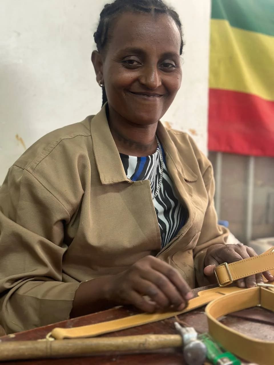 An artisan seated at her bench with leather straps, the Ethiopian flag behind her.