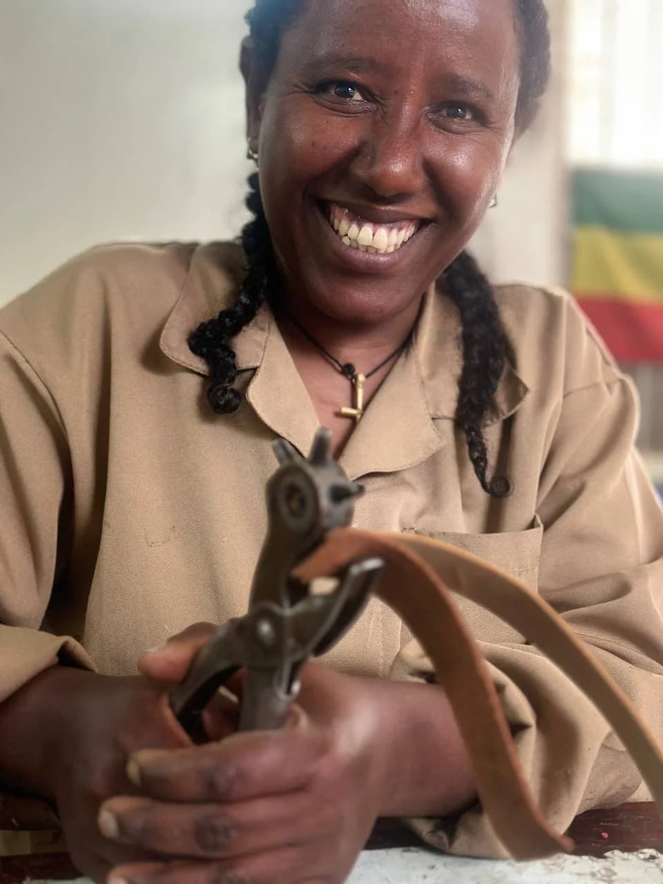 An artisan laughing as she holds leather-punch pliers and a length of leather strap.