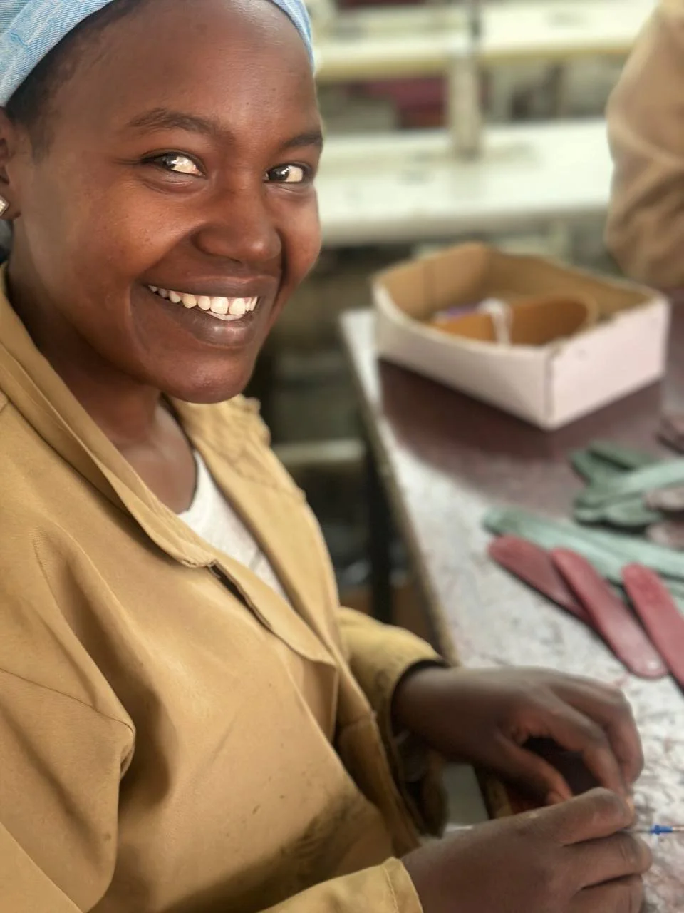 A smiling artisan at her workbench with strips of cut leather beside her.